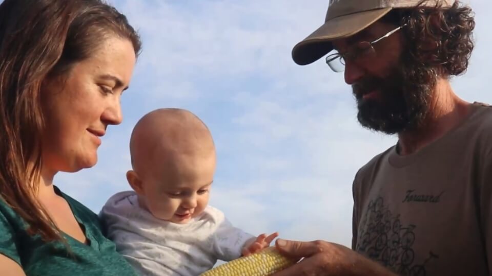 family photo of a man, woman, and child, holding a corn cob