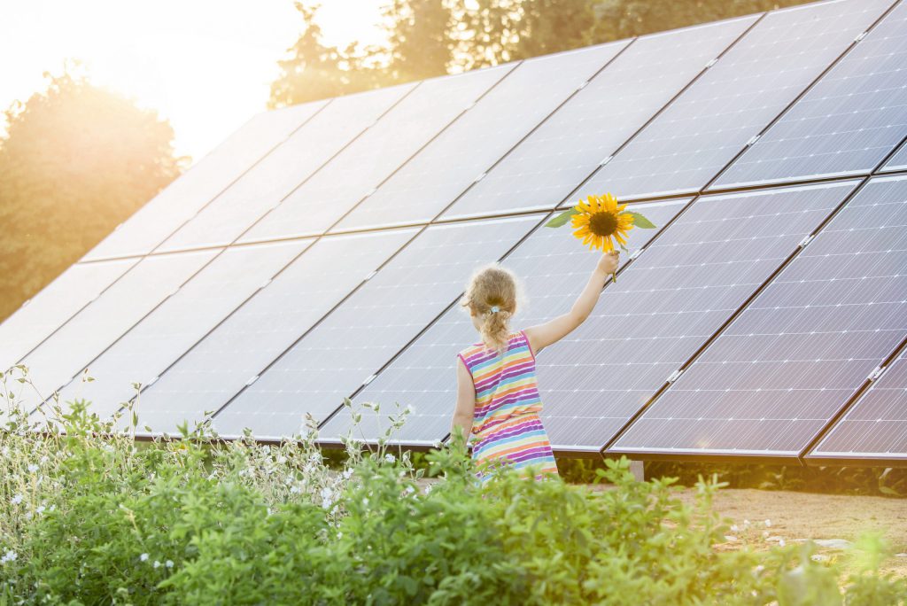 Young girl holding a sunflower stands in front of solar panel