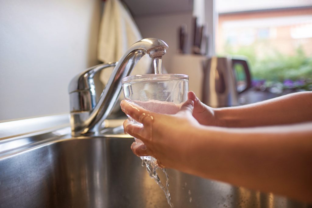 Close up of child's hands, filling glass of fresh water from tap in kitchen