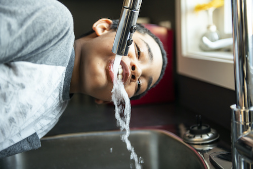 A child drinking water from a kitchen tap
