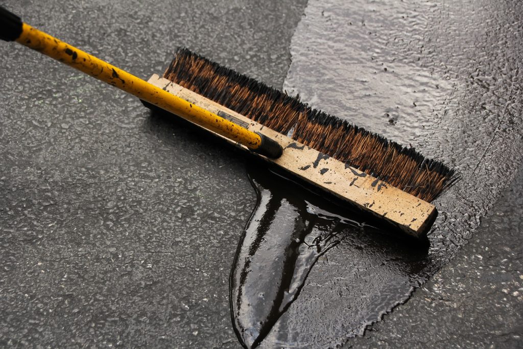 A brush that's used to apply tar sealant in a pile of tar in a driveway