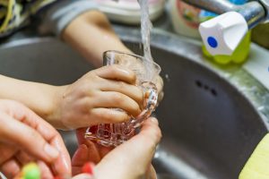 Closeup parent and child hands rinsing dishes in sink