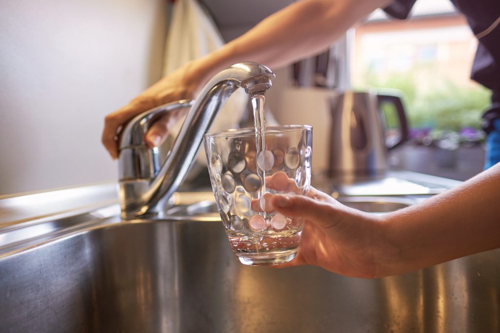 Close up of woman and children hands, pouring glass of fresh water from tap in kitchen