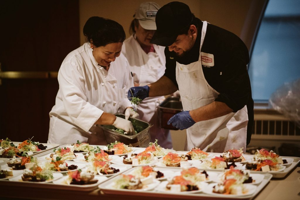 Three chefs preparing at least thirty plates of fancy and delicous looking food