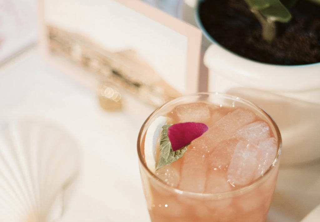 A table with a cocktail garnished with a mint leaf and flower petal