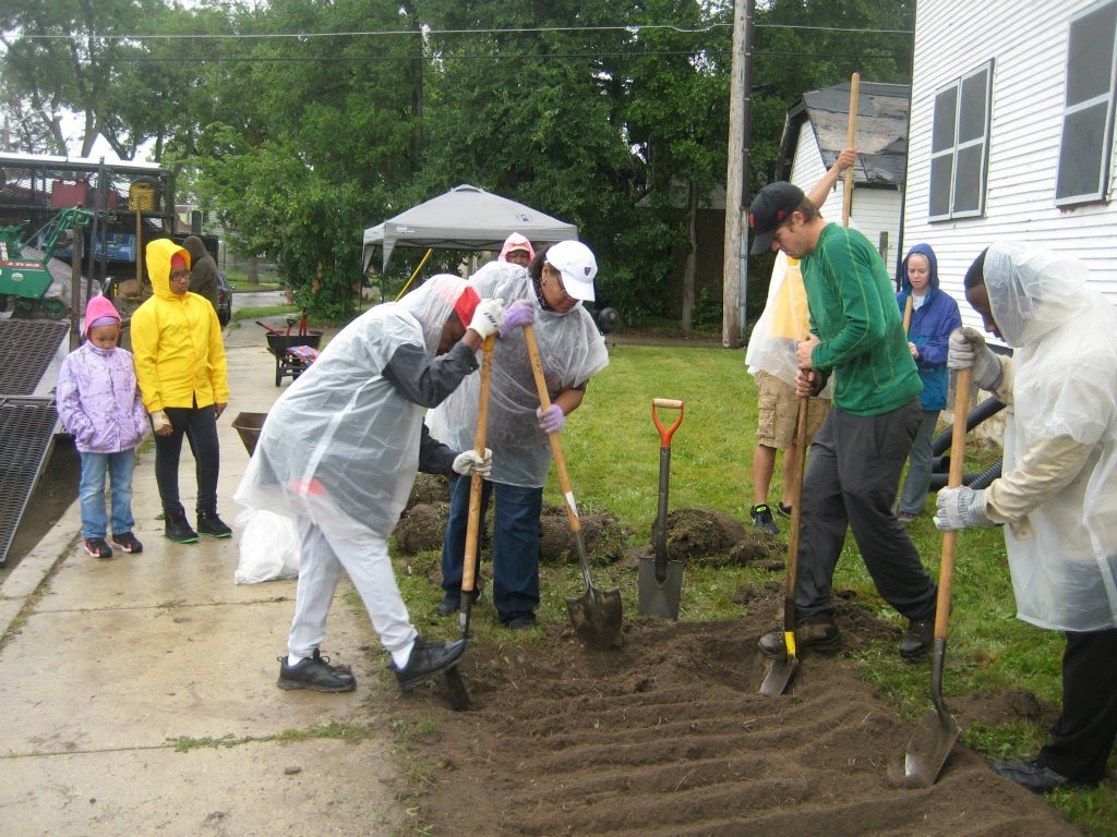 Milwaukee community members using shovels to dig up turf in a yard in the rain