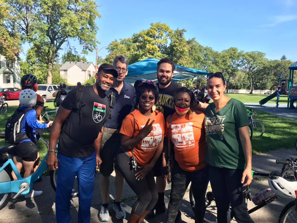 A group of community members posing in front of a tent at a bicycle event at a children's park