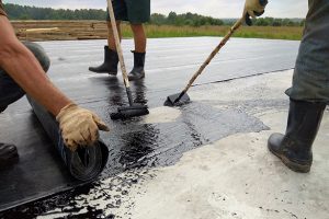 Roofer worker painting bitumen praimer at concrete surface by the roller brush Waterproofing 2018