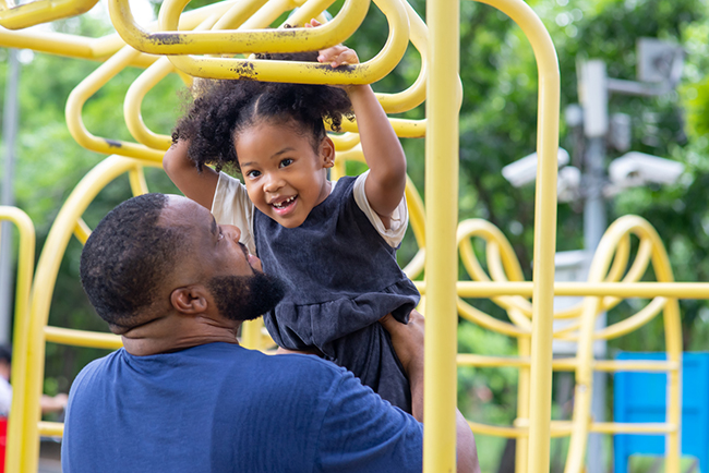 Happy African father carrying little daughter playing at playground in the park.