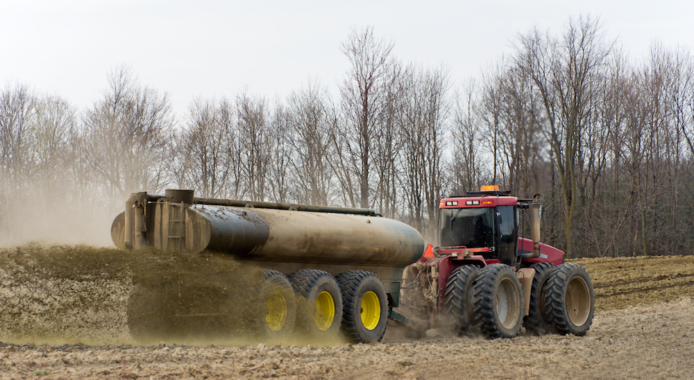 A farmer with a large tractor spreading liquid manure on a ploughed field on an overcast spring day.
