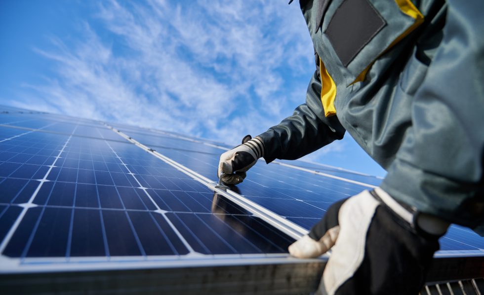 A person wearing a winter coat and work gloves installing a solar panel outdoors
