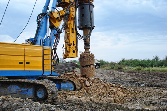 A piece of drilling machinery in a field of dirt near a row of trees