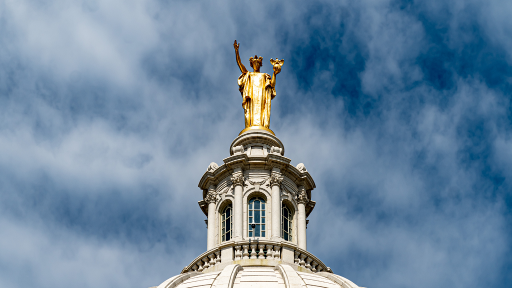 The top of the Wisconsin State Capitol in front of a cloudy backdrop.