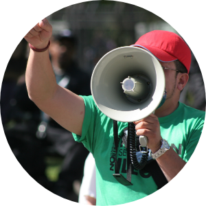 A man wearing a green shirt holding a megaphone at a protest rally