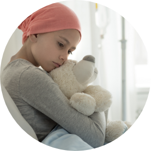 A child with cancer sits in a hospital bed hugging a stuffed bear