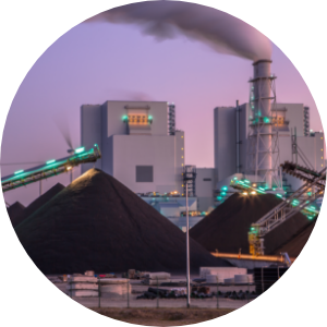 A coal plant with heaping piles of coal in the foreground and a smoke stack in the background