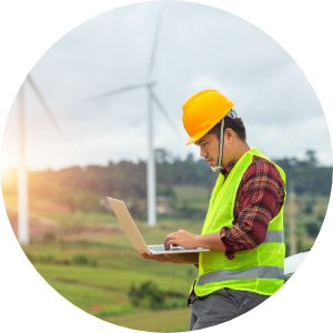 A wind turbine worker holding a laptop and wearing a hard hat